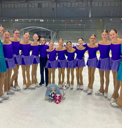 Tým krasobruslařek ve fialových šatech na ledě